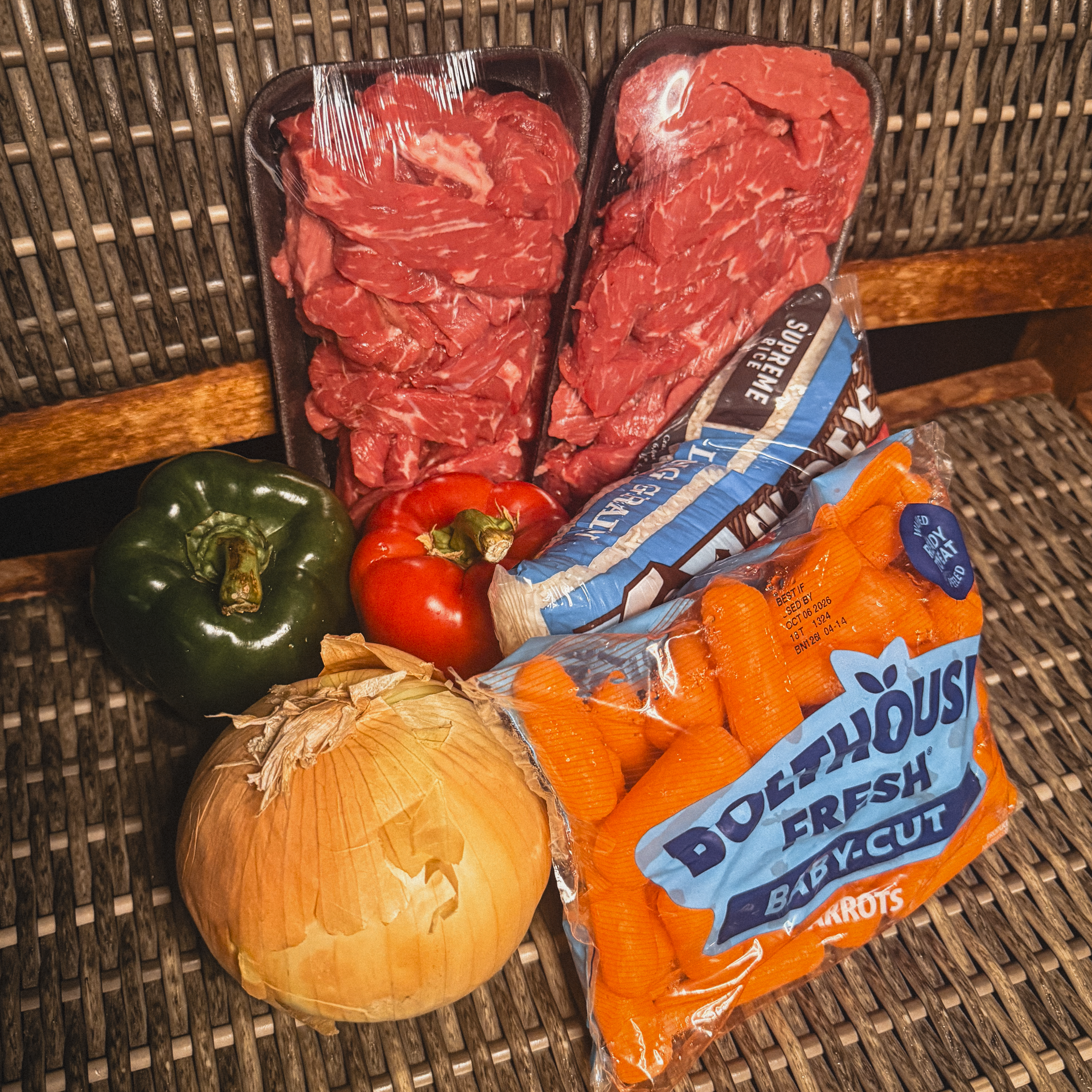 Two trays of Lil Butcher Shoppe beef sliced for stir fry with bell peppers, an onion, baby carrots and long grain rice