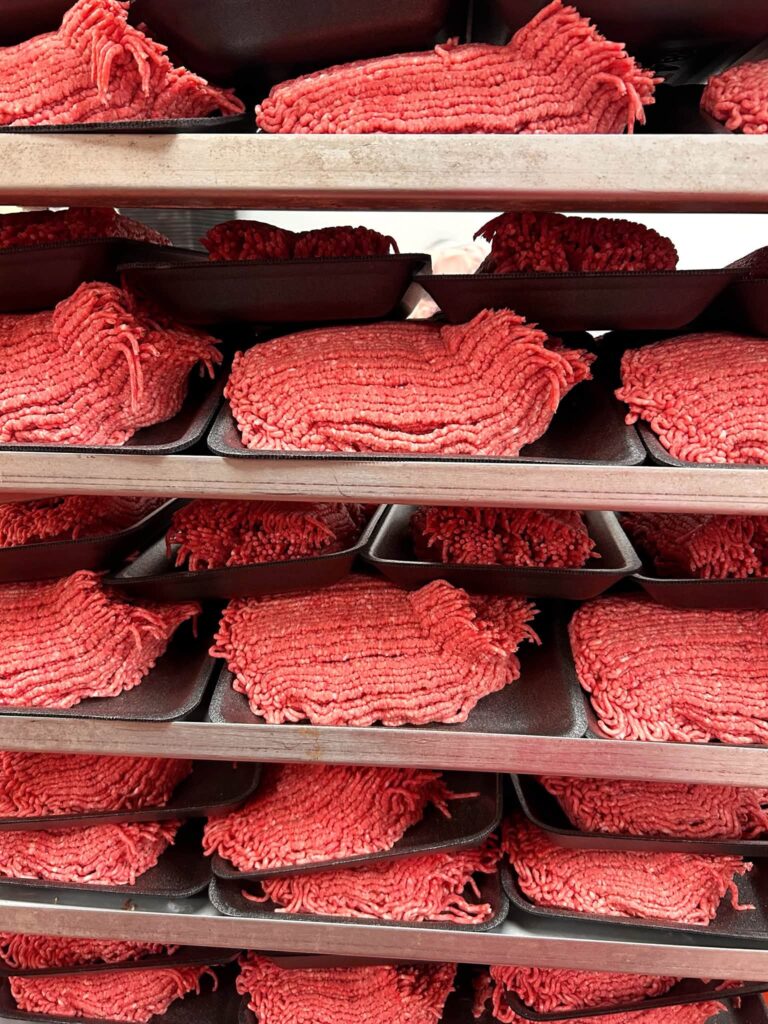 Family packs of fresh ground beef stacked on racks at Lil Butcher Shoppe